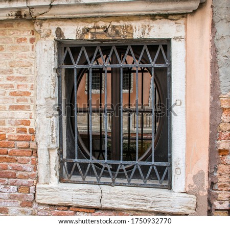 reflections of the city on the glasses of an oval window with railings in Venice, Italy