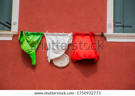 Italian flag created with three t-shirts on red wall and green windows in Venice, Italy