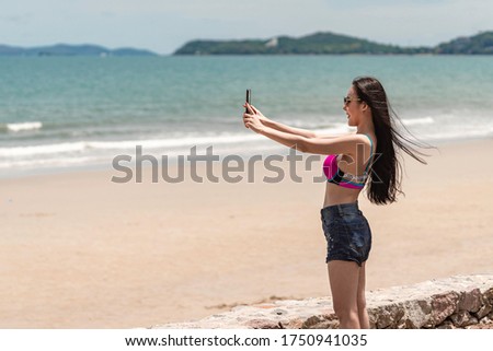 Beautiful young Asian woman in pink bikini take selfie on beach. Copy space concept for solo outdoor activity and travel in summer 