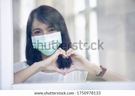 Virus mask Asian woman and make a symbol with their heart at the window of the house, prevention COVID-19