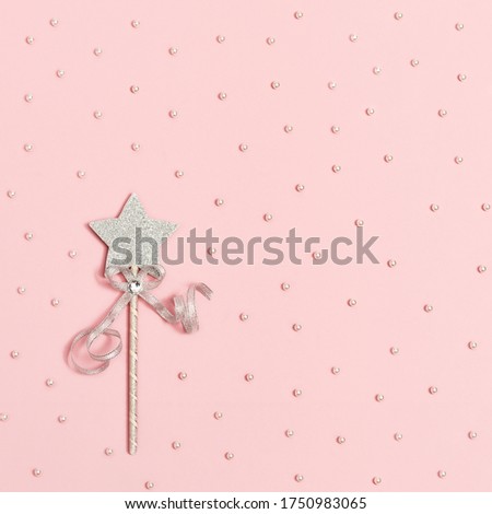 Magic wand, bright silver star with shine on light pink background with white beads. Minimal holiday concept. Copy space.