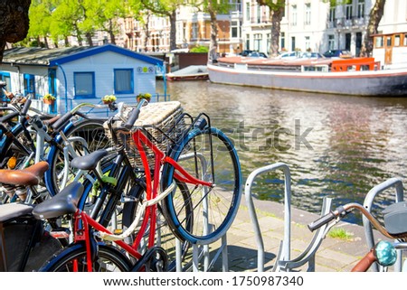 Bicycles parking lot in Amsterdam, Netherlands against a canal during summer sunny day. Amsterdam postcard iconic view. Tourism concept