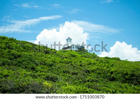 Picture of a green hill, a blue sky and a white little house in the middle.