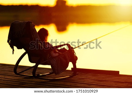 Cute little child girl in in chair on wooden pier at lake. Family leisure activity during summer sunny day sunset.