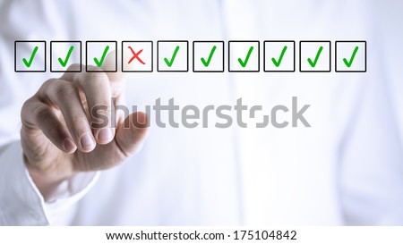 Man selecting a red cross in a box from a line of green check marks or ticks in boxes on a virtual screen conceptual of individuality, quality, failure and negativity