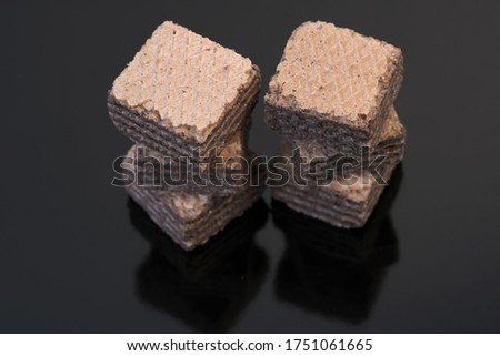 Small square pieces of sweet waffles with chocolate filling against black background close-up macro photo