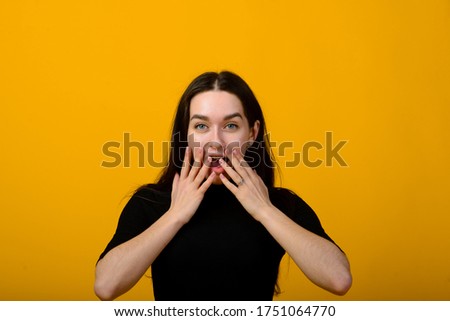 Wow. Beautiful female half-length front portrait isolated on yellow studio backgroud. Young emotional surprised woman standing with open mouth. Human emotions, facial expression concept.