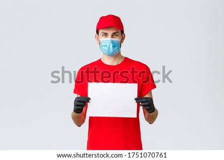 Covid-19, self-quarantine, online shopping and shipping concept. Express delivery guy during coronavirus tell stay safe home, buy internet, holding blank piece paper for your info, wear face mask