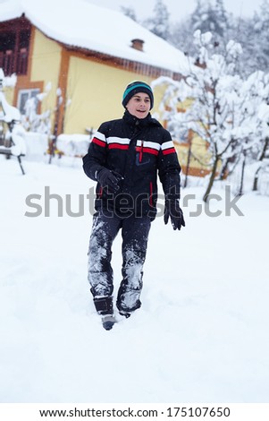 Happy teenage boy walking through the snow, with house and trees in the background