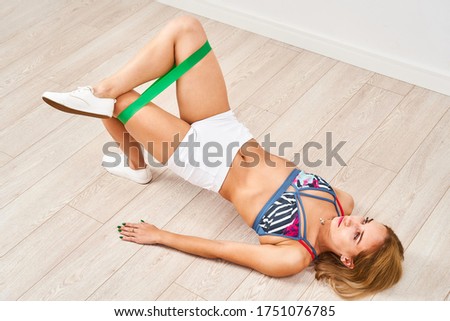 Young athletic woman does exercises with a fitness elastic band. Wants to tighten figure. A young girl in sports clothes does exercises for leg muscles, lying on floor. Exercise for elastic buttocks.