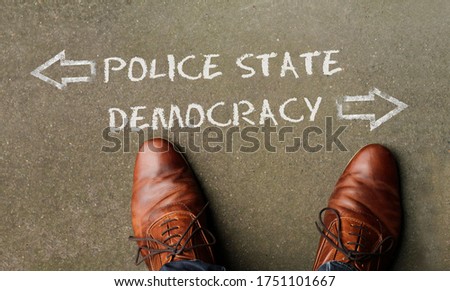 Top view on a man standing in front of the words "Police State" and "Democracy" with arrows pointing to the left and right side of the picture