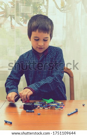The boy playing an electric constructor. The child is played by intellectual toys. A boy in a blue shirt masters electronics. The concept of early development of children. vertical photo. toned