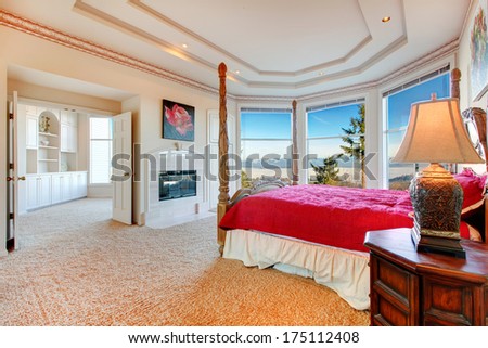 Stunning luxury master bedroom with rich bedroom furniture and amazing angled glass wall overlooking picturesque view