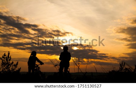 Silhouette of mother with her daughter and two bicycle. healthy lifestyle. figure of mom and baby biking at sunset. people looking at sunset horizon. back rear view.