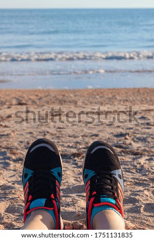 Young tourist woman feet in sport footwear relaxing after hiking on sea sand beach.Adventure backdrop for inspiration, motivational quotes, blog posts, text sign. POV shot of human legs on a sunny day
