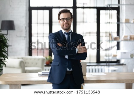 Portrait of smiling successful Caucasian businessman in formal suit glasses stand posing in modern office, happy young male boss or CEO look at camera, show confidence and power, leadership concept Royalty-Free Stock Photo #1751133548