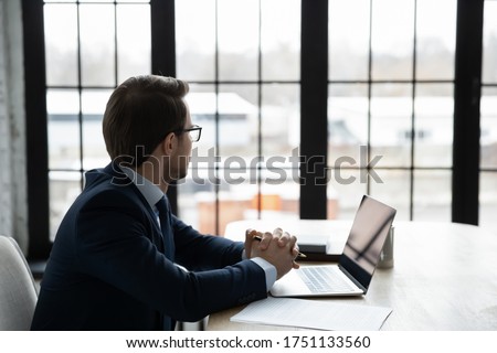Thoughtful successful businessman look in window distance planning or pondering about business startup, pensive male boss or CEO in suit lost in thoughts thinking considering, make solution Royalty-Free Stock Photo #1751133560