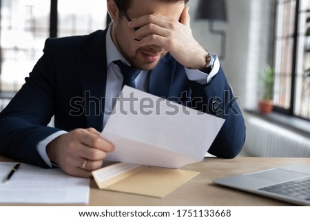 Upset male employer or boss sit at desk feel distressed disappointed reading post paper correspondence, unhappy employee frustrated by postal paperwork, get dismissal notice, fired, failure concept Royalty-Free Stock Photo #1751133668