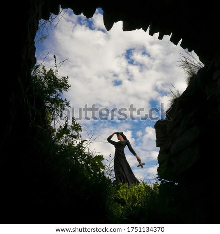 Beautiful middle age  nun in black cassock and cloak is standing with cross in her hands on blue cloudy sky background. summertime season.