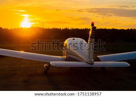 Rear view of a parked small plane on a sunset background. A silhouette of a grounded private jet at dusk. Piper Cherokee individual propeller aircraft Royalty-Free Stock Photo #1751138957