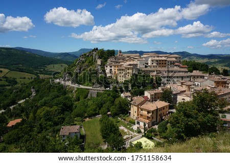 Wonderful view of old small town on the hill during summer surrounded by young green plants and mountains with blue and clouds sky background