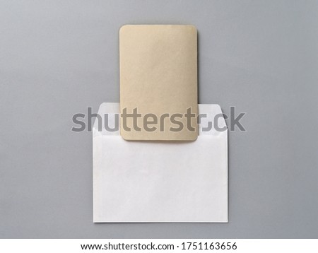 An empty Kraft brown card for an invitation or greeting and a white paper envelope on a gray textured background. Mock-up. Stylized stock photos. The view from the top.
