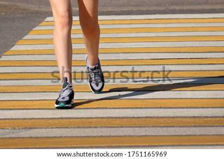 Slim girl crossing the street, female legs in sneakers on pedestrian crossing. Concept of road safety, running woman in summer city