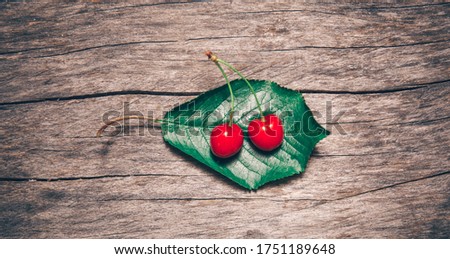 Two cherries on a green leaf on an old wooden background. View from above.