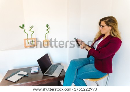 Stock photo of woman using laptop and mobile phone at home. She is touching the screen of telephone