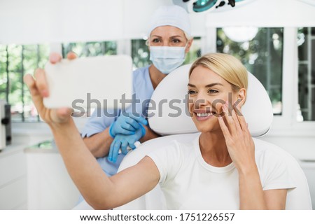 Beautiful and happy blonde woman at beauty medical clinic. She is sitting and talking with female doctor about face esthetics treatment. Royalty-Free Stock Photo #1751226557