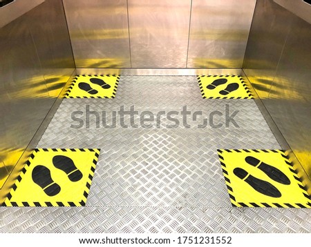 Social distancing for COVID-19 coronavirus crisis prevention with yellow footprint sign with text caution to respect social distance, in public elevator (lift) area