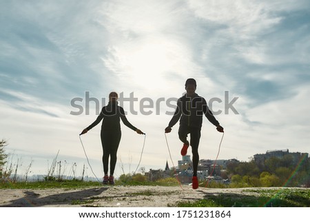 Healthy and sporty people. Young african fitness couple in sportswear exercising with skipping rope outdoors in nature against blurred city background. Sport, training, workout. Healthy lifestyle