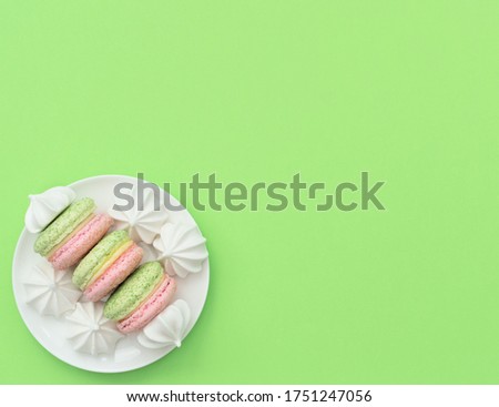 Delicious macarons with white merengues on white plate on green background. Happy day, breakfast, good morning concepts. Time for tea. Greeting or invitation card. Flat lay style with copy space.
