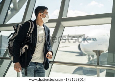 Asian traveler business man wearing face mask waiting to board into airplane, standing in departure terminal in airport. Male passenger traveling by plane transportation during covid19 virus pandemic. Royalty-Free Stock Photo #1751259014