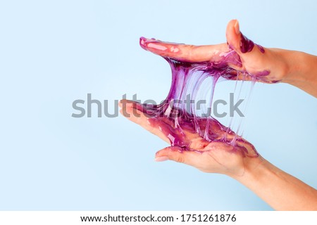 Young girl hands with sticky purple slime on blue background, liquid wax for depilation, conceptual flyer banner with copy space, antistress relax, modern kids hobby oddly satisfying semi surreal asmr Royalty-Free Stock Photo #1751261876