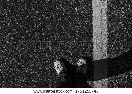 black pavement street with white line and legs of person with white sneakers overhead image
