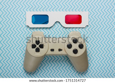 Anaglyph disposable paper 3d glasses and retro gamepad on blue background. Top view