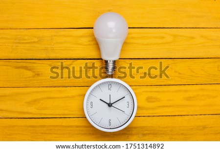 Clock with light bulb on yellow wooden background. I have an idea! Minimalism. Top view