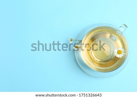 Delicious chamomile tea in glass cup on light blue background, top view. Space for text