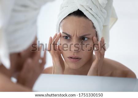 Close up unhappy woman wearing white bath towel checking skin after shower, looking in mirror, worried about mimic wrinkle or acne, touching face skin, facial cosmetology, treatment, skincare concept Royalty-Free Stock Photo #1751330150
