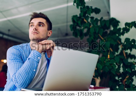 Contemplative male freelancer sitting at table with netbook computer and thinking on idea for web design, pensive Caucasian man thoughtful looking away pondering on system update for laptop device