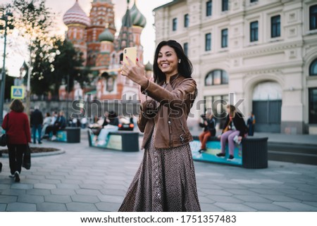 Cheerful female travel blogger shooting influence vlog with web sightseeing during solo vacations in Moscow, smiling Asian tourist in earbuds making international video call for communicate in roaming