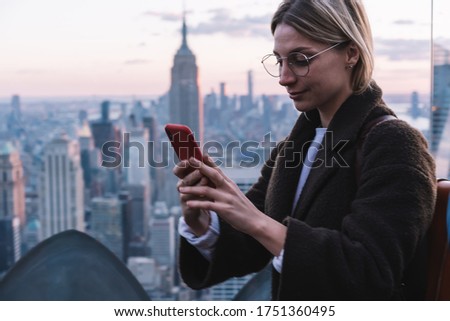 Caucasian female tourist using cellular device for social messaging with followers connecting to roaming internet during solo travel journey for visiting New York, youthful hipster girl browsing web