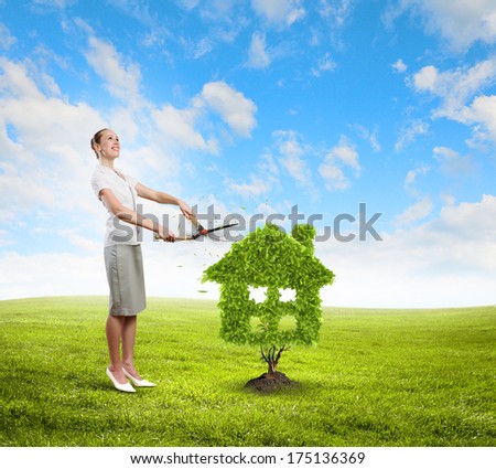Young attractive businesswoman cutting lawn in shape of house
