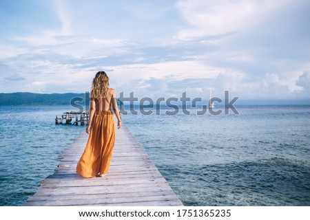 Back view of female tourist enjoying resort vacations in paradise nature environment, woman in stylish sundress walking at pier recreating during solo travelling for visiting Bora Bora island Royalty-Free Stock Photo #1751365235