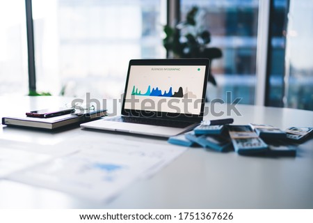 Electronic netbook technology with business infographics on laptop screen and money wat stands on table desk in office enterprise, modern computer with graphic analytic charts on web dashboard
