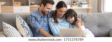 Couple and little daughter sit on sofa using pc watching cartoons on-line, surfing internet, buying via e-commerce web sites, spend weekend at home. Horizontal photo banner for website header design