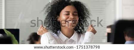 Excited African employee sitting in office received long awaited great news feels happy, reward, job advancement, promotion and career growth concept. Horizontal photo banner for website header design Royalty-Free Stock Photo #1751378798