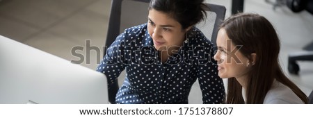 Multi ethnic female colleagues sit at workplace working together looks at pc screen use corporate program, apprentice listen mentor, teamwork concept. Horizontal photo banner for website header design