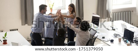 Group of multi ethnic employees gathered in co-working celebrating successful project accomplishment giving high five. Teamwork, teambuilding concept. Horizontal photo banner for website header design